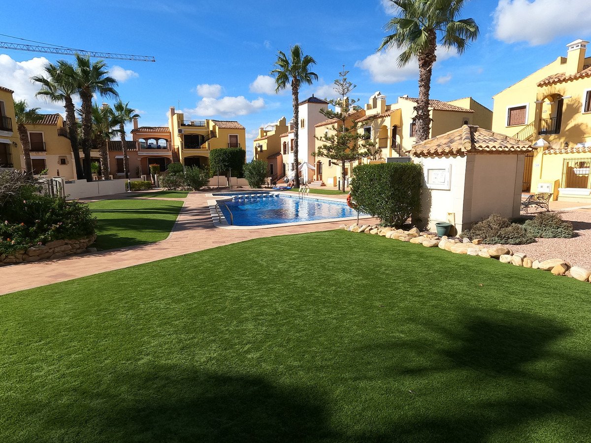 A residential complex with a blue swimming pool, lush green lawn, and palm trees under a bright blue sky.
