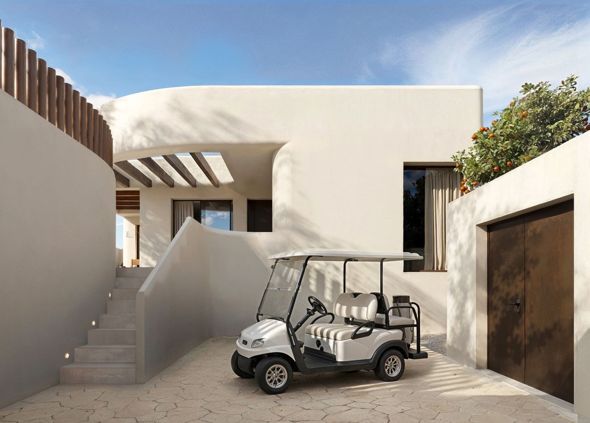 A modern villa exterior with a golf cart parked in front, featuring white stucco walls and stone paving.