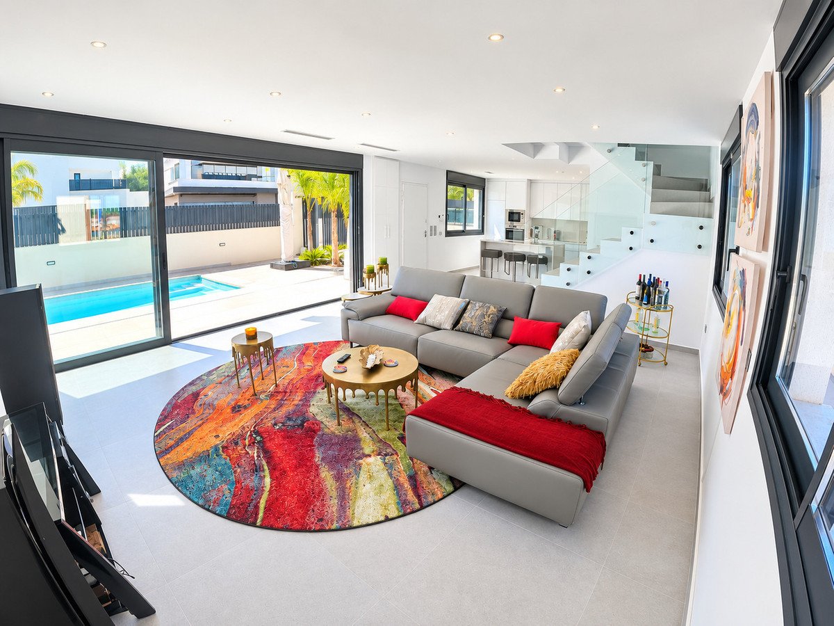 Modern living room with a grey sectional sofa, a colorful rug, and sliding glass doors opening to a swimming pool.