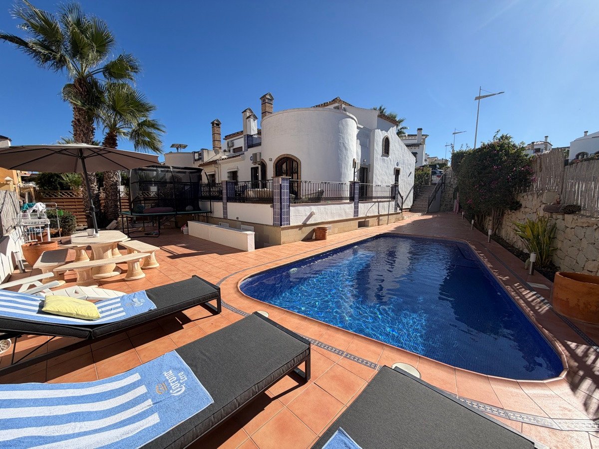 A beautiful villa with a private swimming pool, lounge chairs, dining area, and palm trees under a clear blue sky.