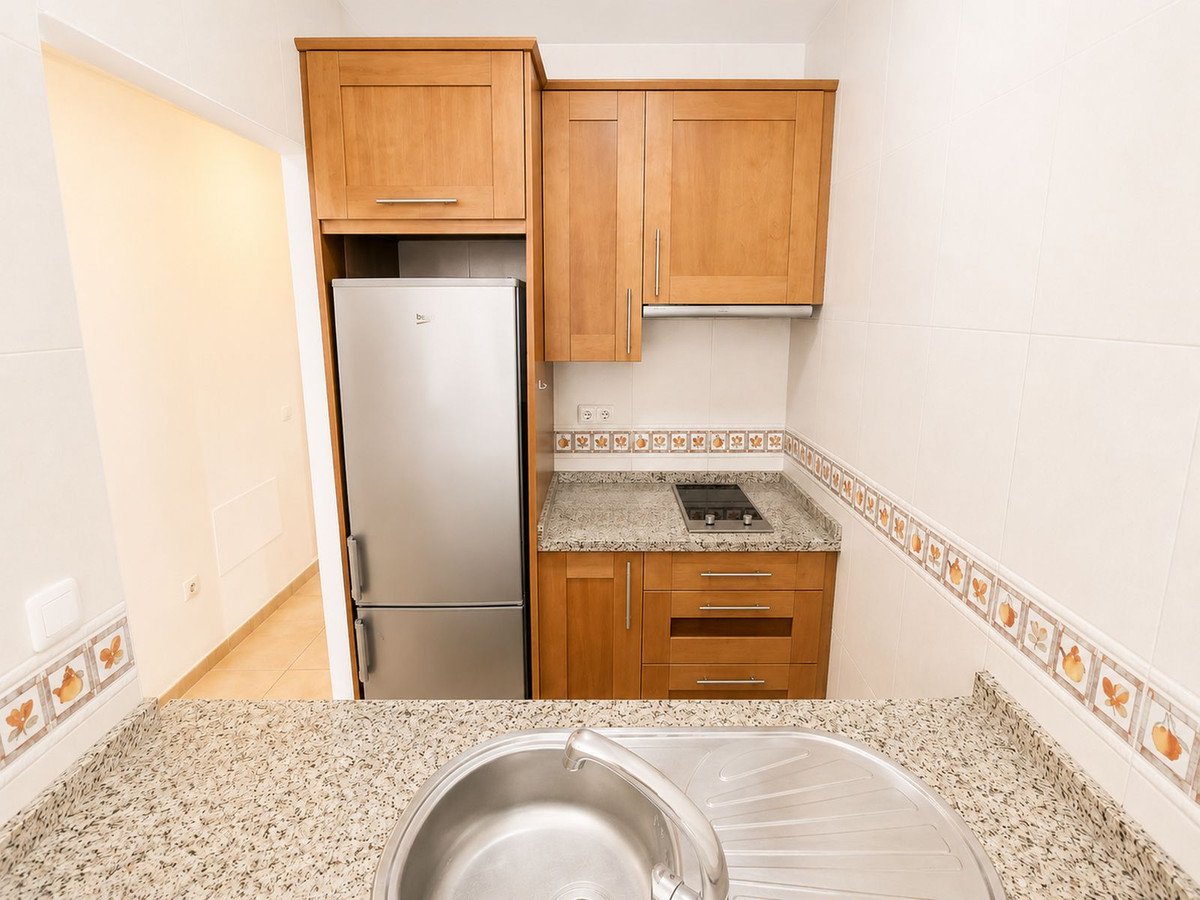 Compact kitchen with wooden cabinets, granite countertops, stainless steel sink, and refrigerator.