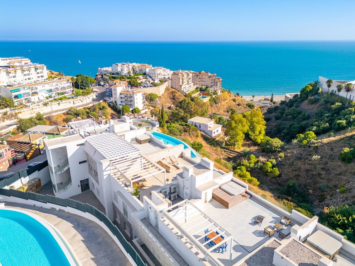 A modern villa with multiple swimming pools and a hot tub, overlooking the sea and a distant beach.