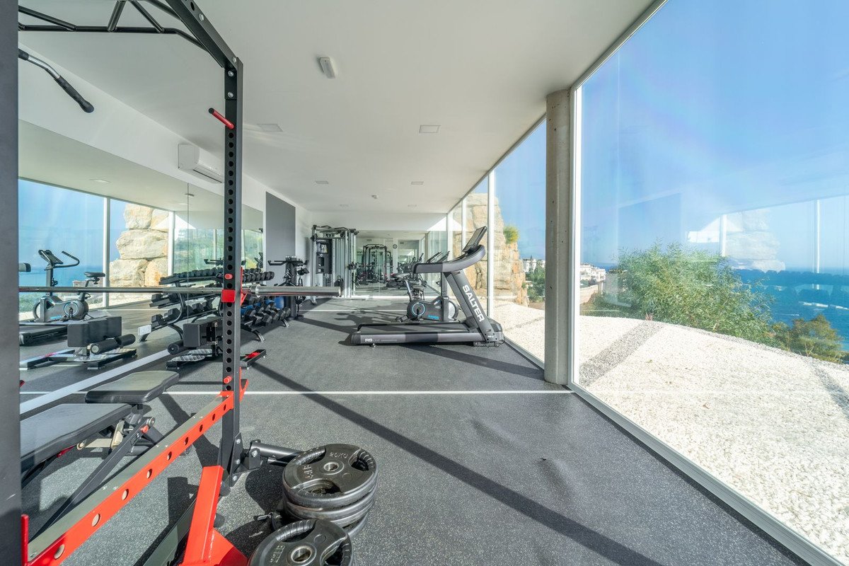 Modern gym with treadmills, weights, and large windows offering a stunning ocean and coastal view.