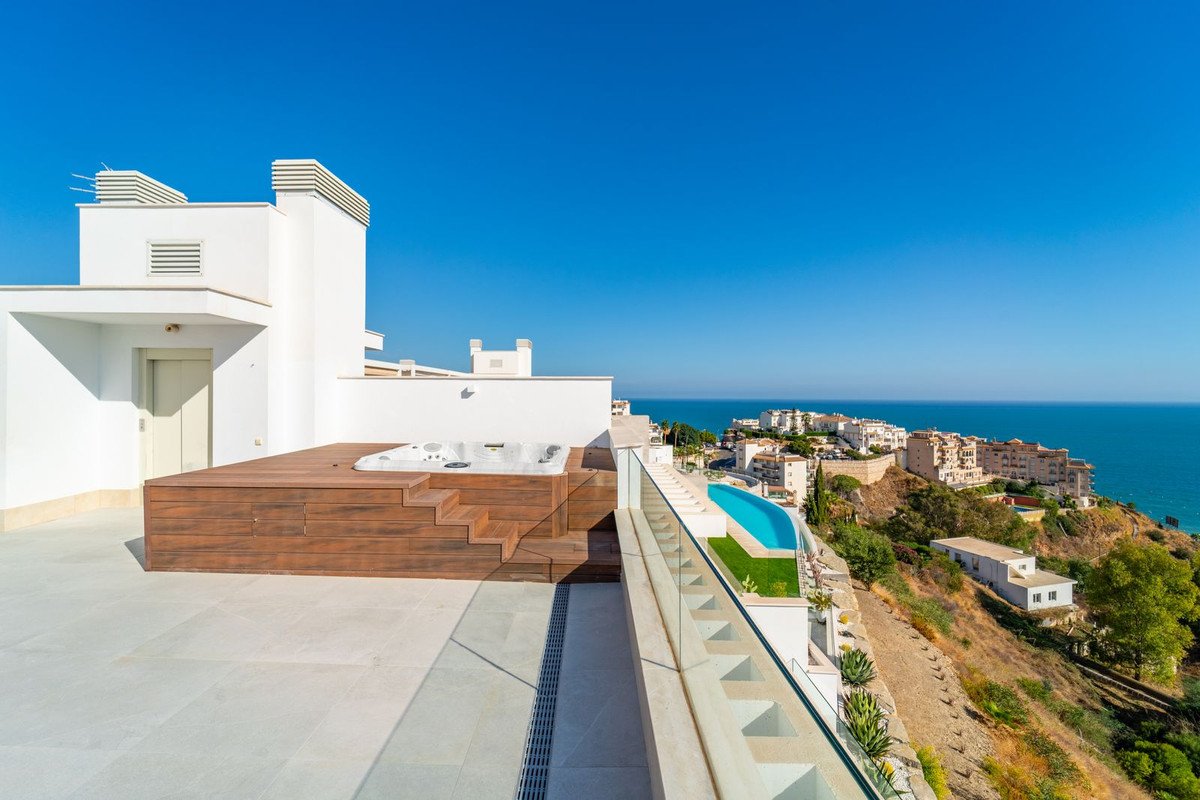 Modern terrace with jacuzzi, infinity pool, and stunning sea views of a coastal town.