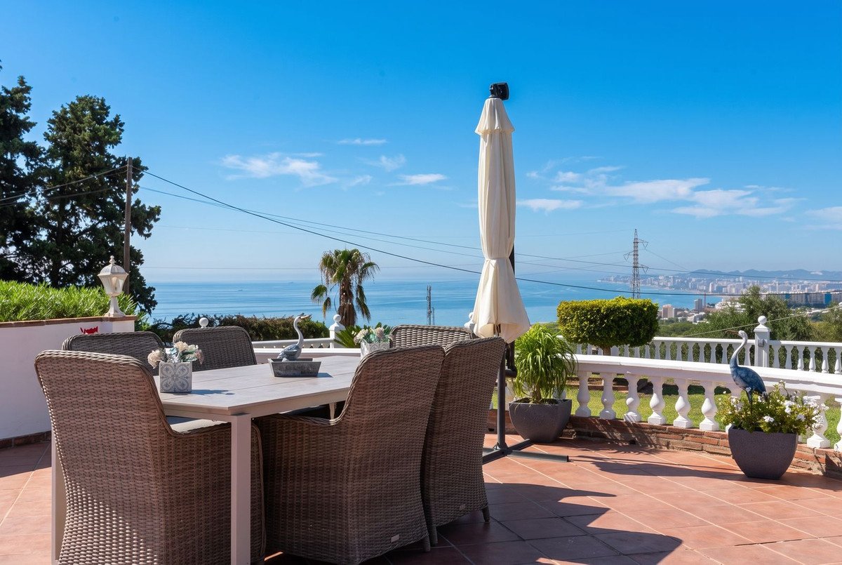 A sunny terrace with a dining set overlooking the sea and a distant cityscape in the distance.