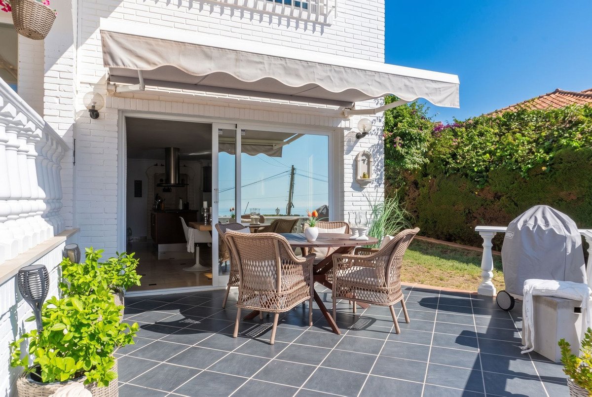 Terrace with rattan dining set and chairs, overlooking the sea. Outdoor space with awning and greenery.