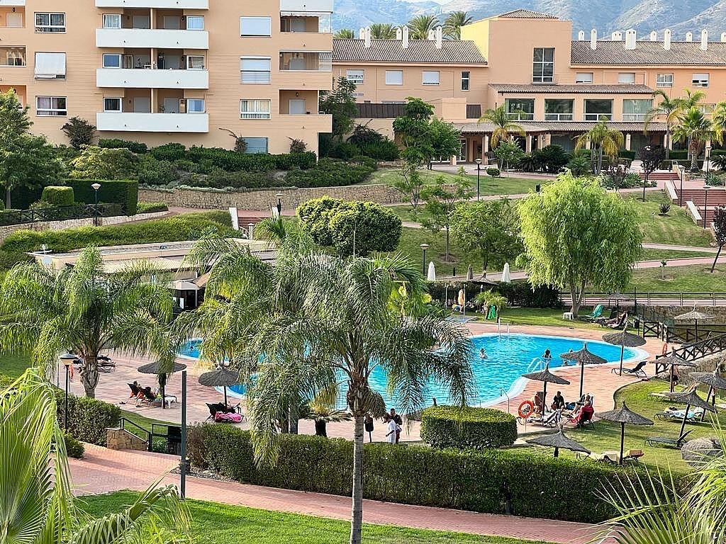 Resort complex with a swimming pool, loungers, umbrellas, and lush green landscaping.