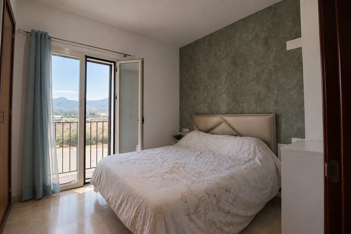Bedroom with a double bed, textured wall, and balcony doors opening to a view of mountains and countryside.