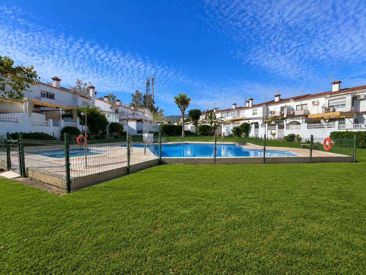 Large swimming pool surrounded by green lawn and white houses under a clear blue sky