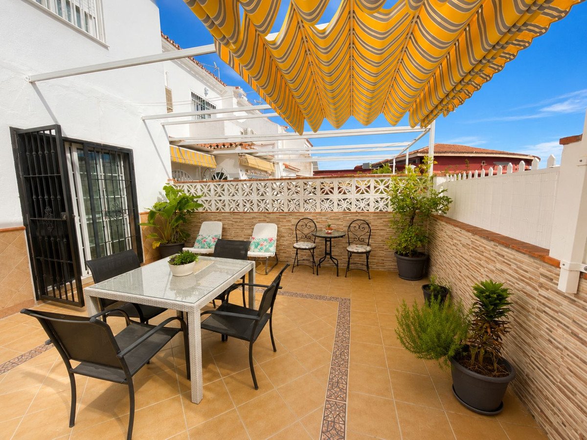 Covered terrace with dining table, chairs, and potted plants under a striped awning