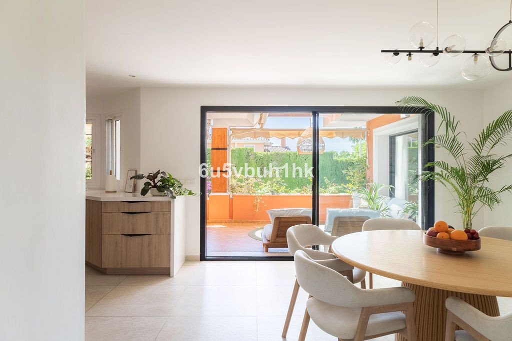 Modern dining area with a round table and chairs, large sliding doors opening to a sunny terrace with outdoor seating.