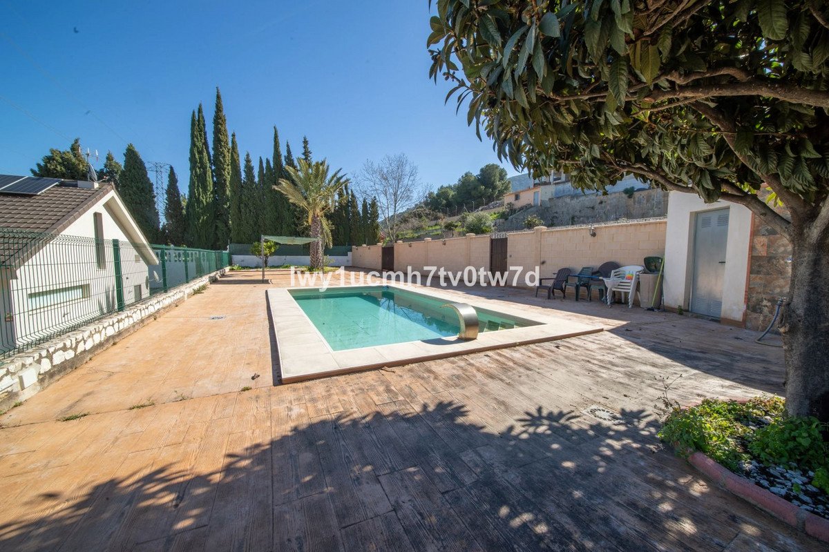 Backyard with swimming pool, patio, trees, and clear blue sky.