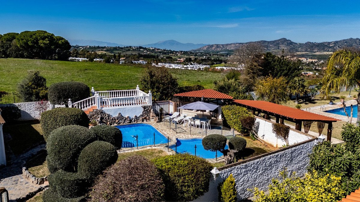 Outdoor area with two swimming pools, covered seating, and a distant view of rolling hills and mountains.