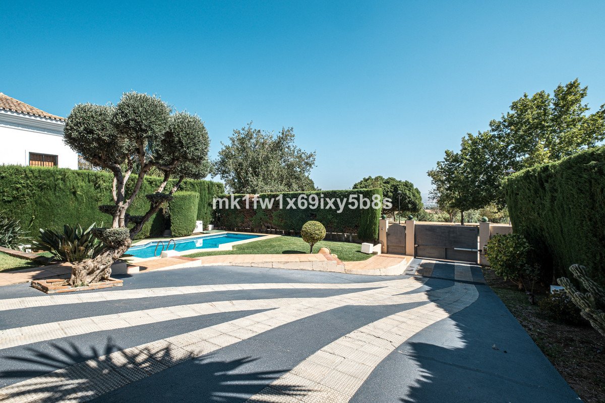 A modern villa with a swimming pool and manicured garden, featuring mature trees and a paved driveway.