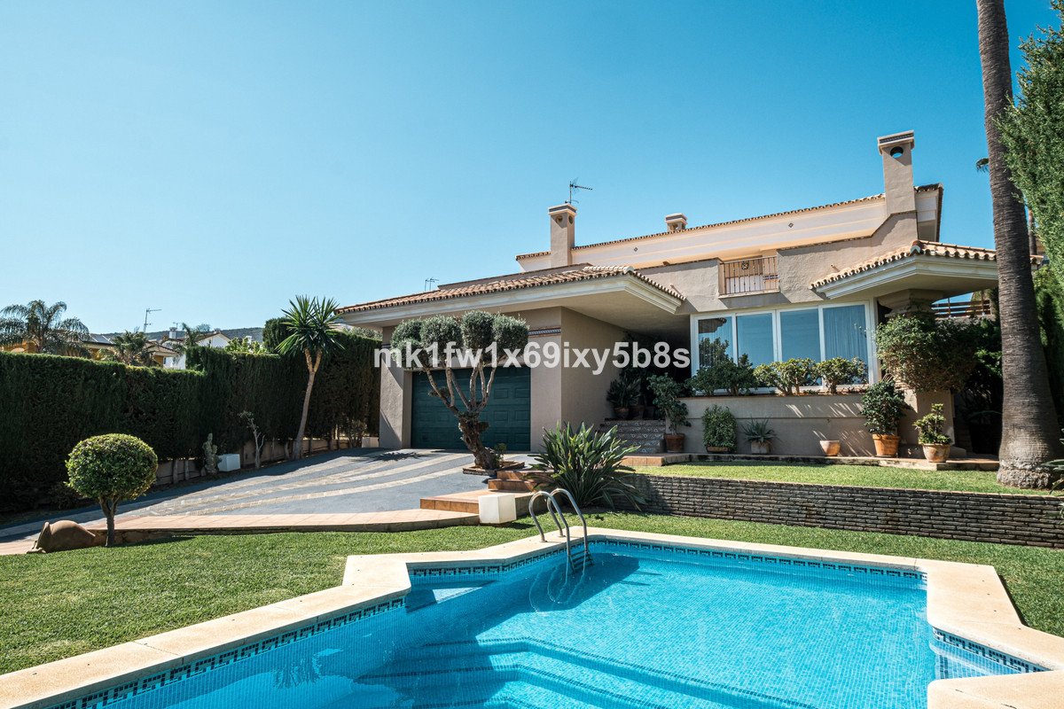 A luxury villa with a swimming pool, green lawn, driveway, and lush garden on a sunny day.