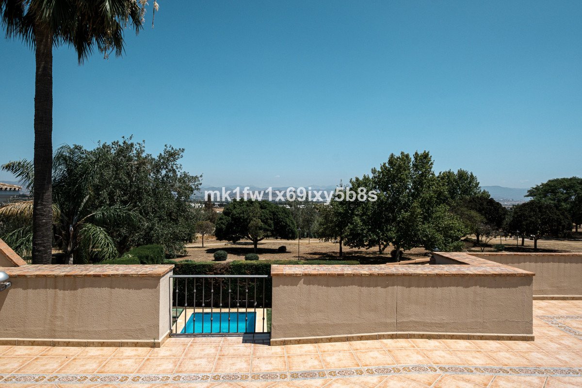 View of a small blue pool with a metal fence, overlooking trees and distant mountains under a clear blue sky.