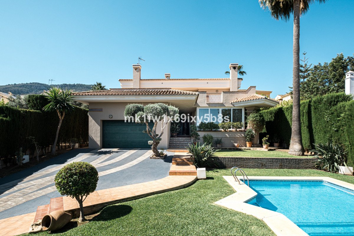 A modern villa with a swimming pool, manicured lawn, and lush garden under a clear blue sky.
