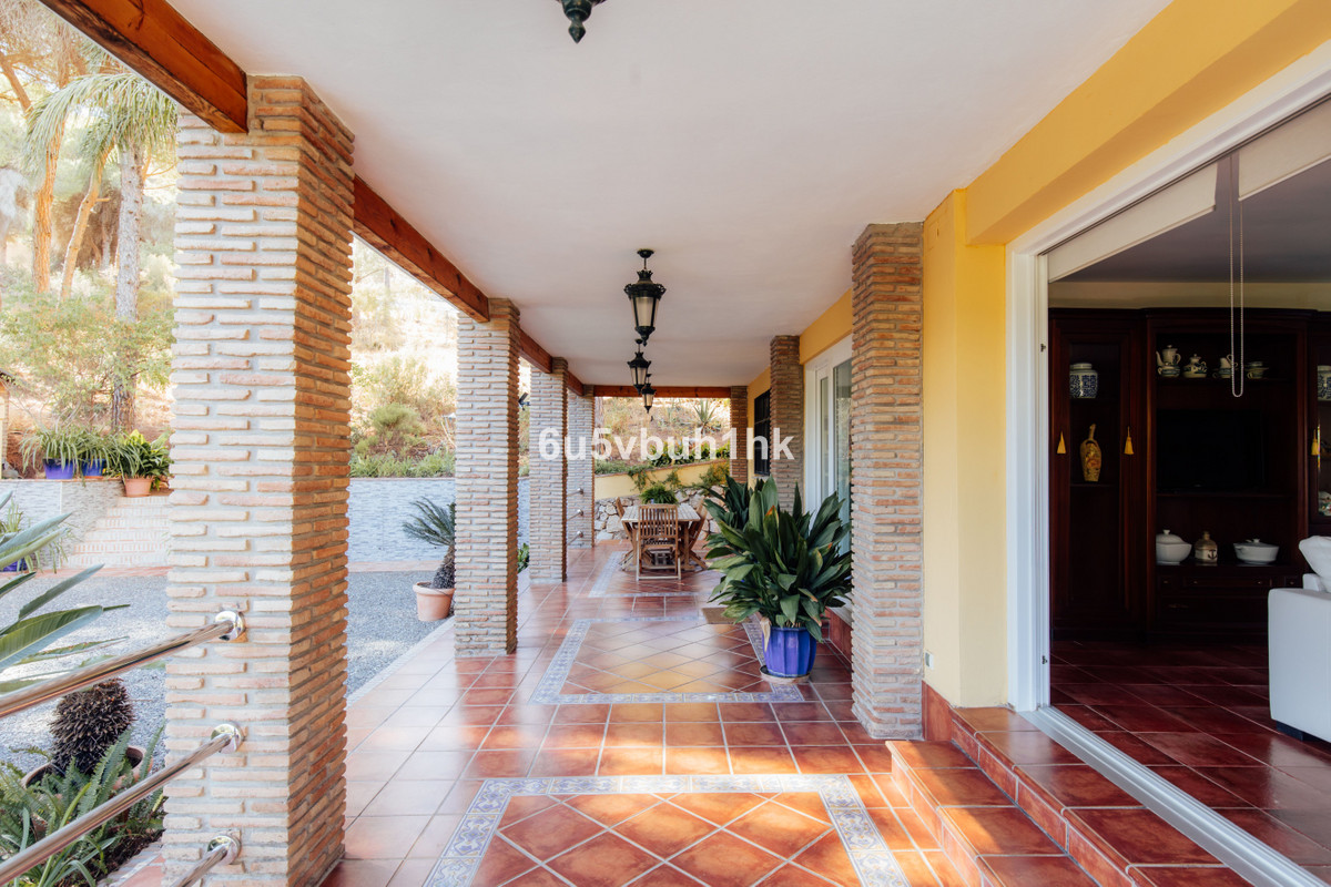 Overdekt terras met stenen pilaren en uitzicht op de tuin.
