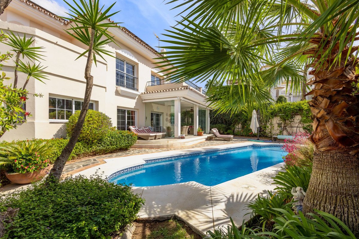 A beautiful villa with a swimming pool, lounge chairs, and lush green landscaping. Covered patio with seating is visible.