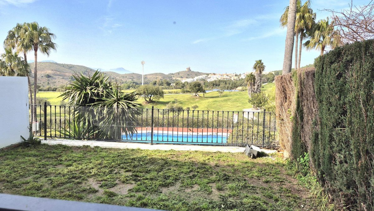 View from a garden with a swimming pool and lush green golf course in the background, surrounded by palm trees and hills.