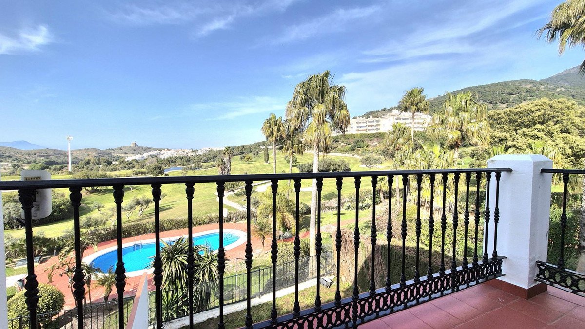 View from a balcony overlooking a golf course with a swimming pool and palm trees, under a blue sky.