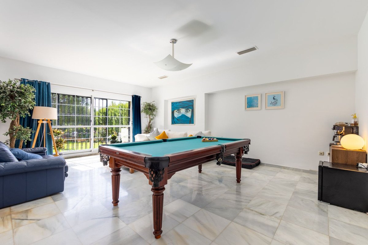 Spacious living room with a pool table, comfortable sofa, and large windows overlooking a lush garden.