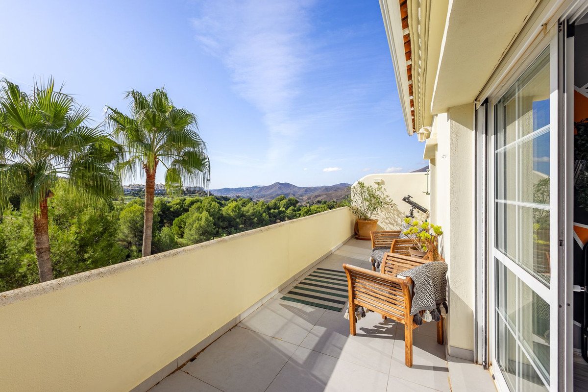 Spacious balcony with seating, offering a scenic view of palm trees and distant mountains under a clear blue sky.