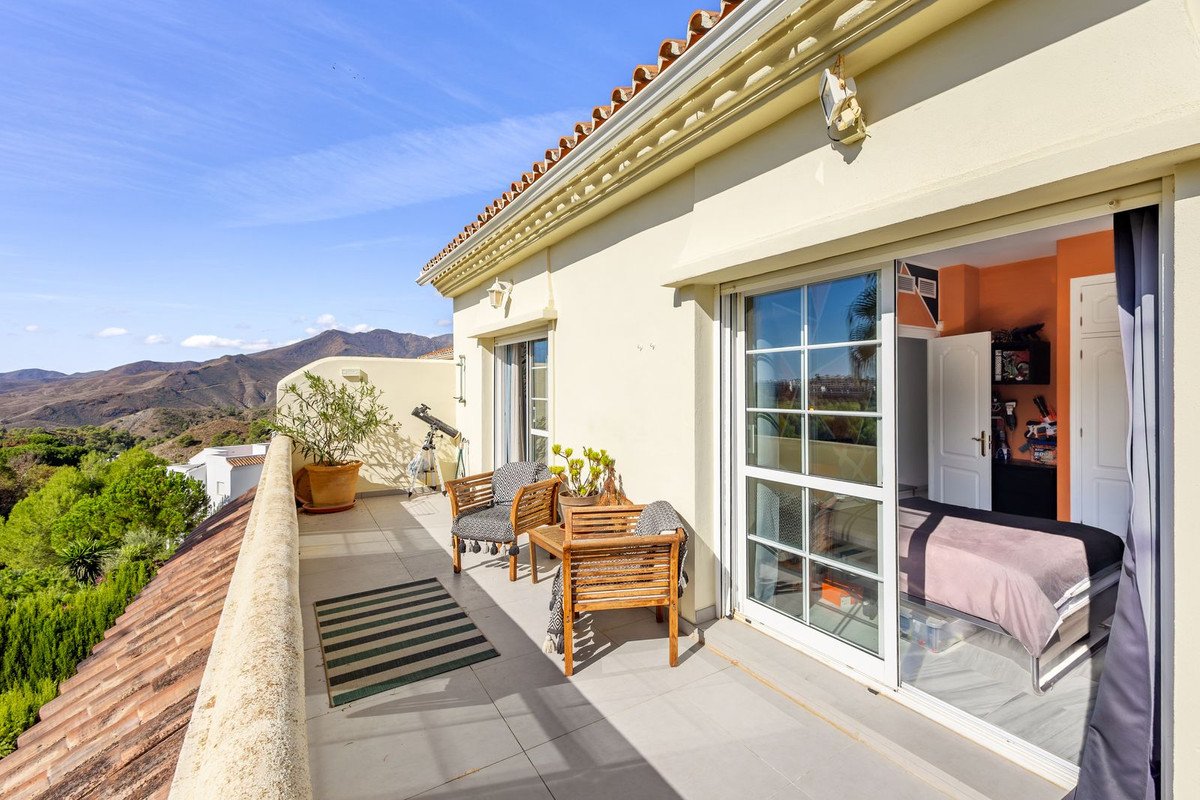 Terrace with seating area and telescope overlooking a lush green landscape and mountains under a clear blue sky.