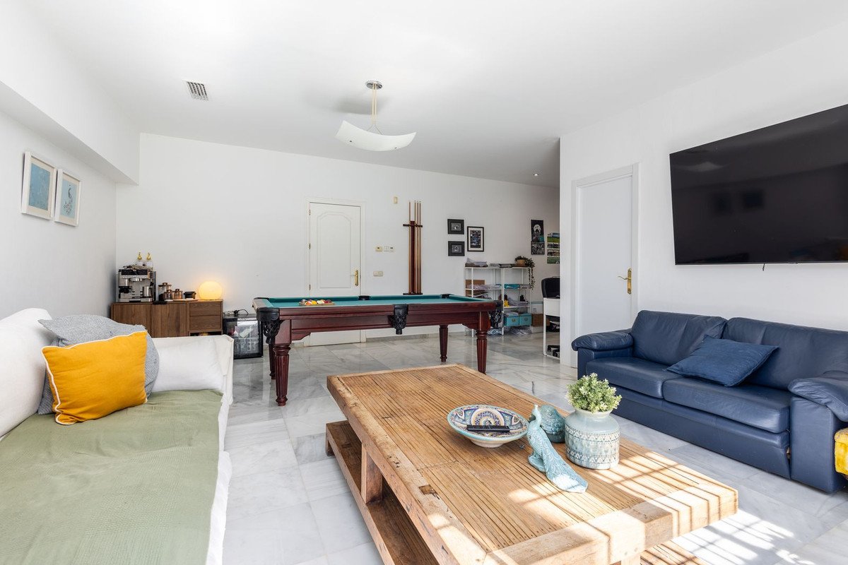 A spacious living room featuring a pool table, a blue leather sofa, a wooden coffee table, and a large television.
