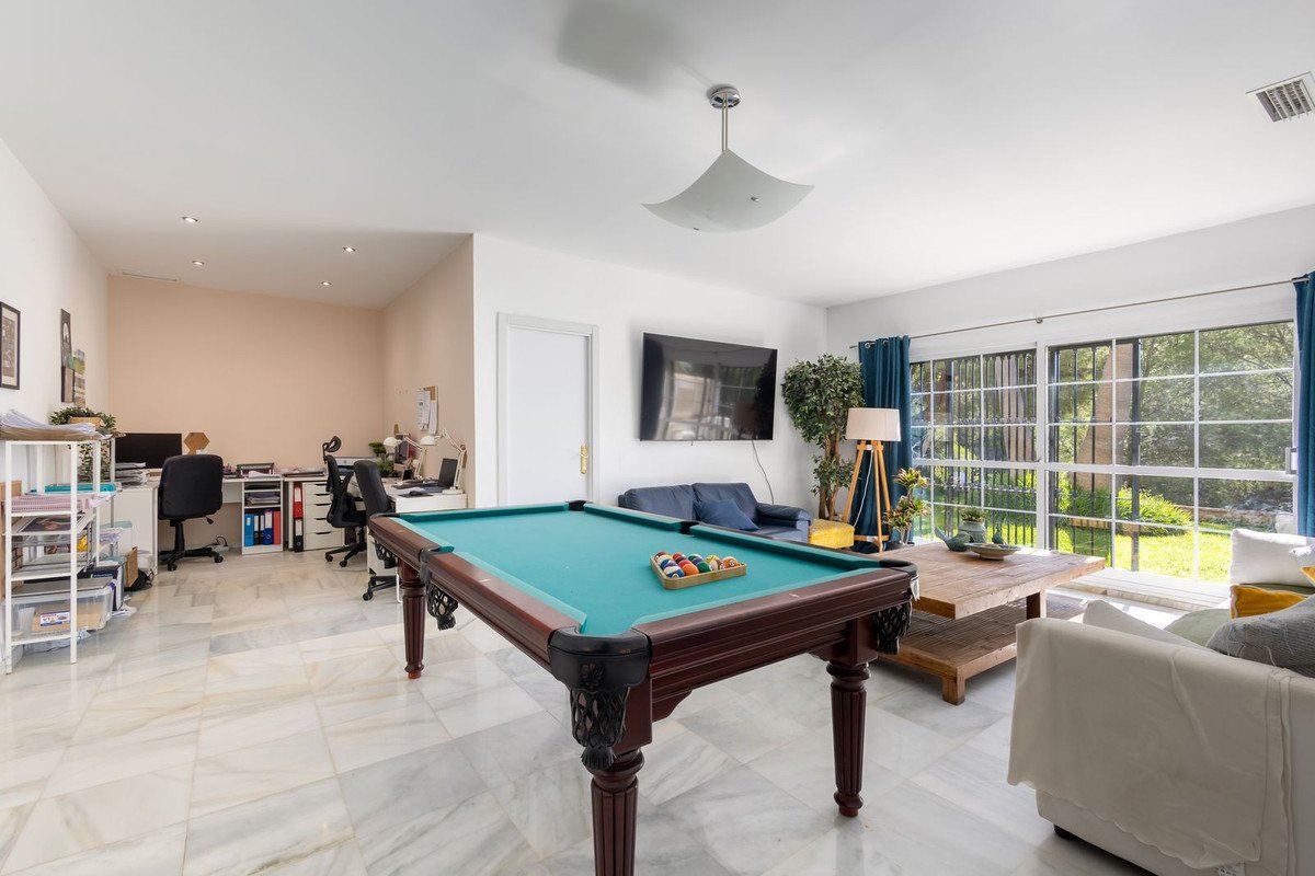 Spacious game room featuring a pool table, two desks with computers, a sofa, and large windows with a garden view.
