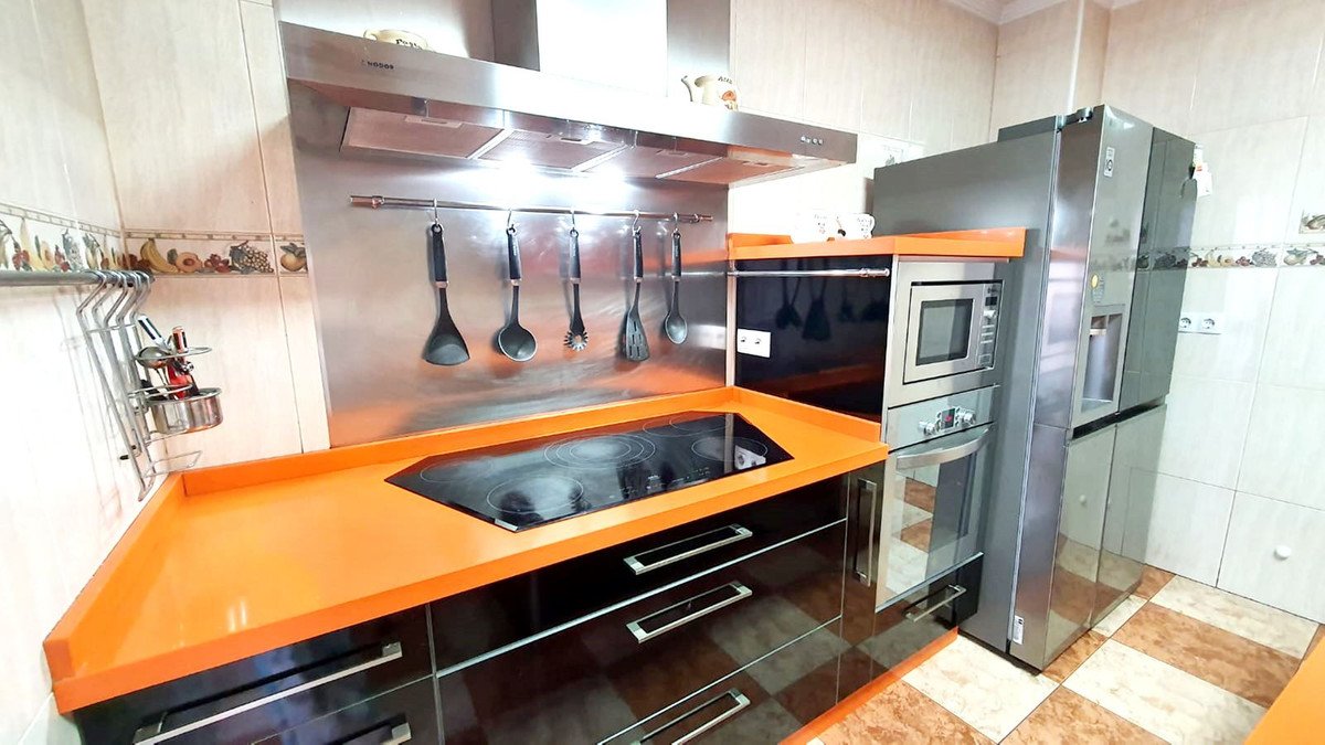 Modern kitchen featuring orange countertops, stainless steel appliances, and hanging utensils