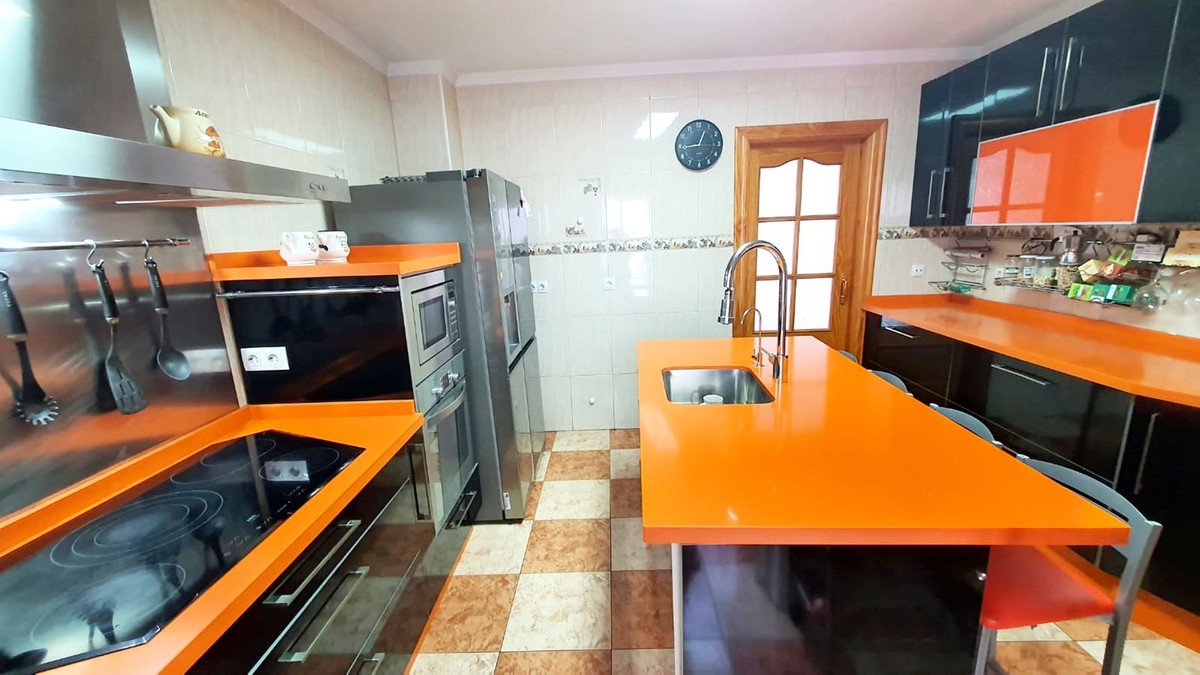 Modern kitchen featuring orange countertops, stainless steel appliances, and a central island with sink