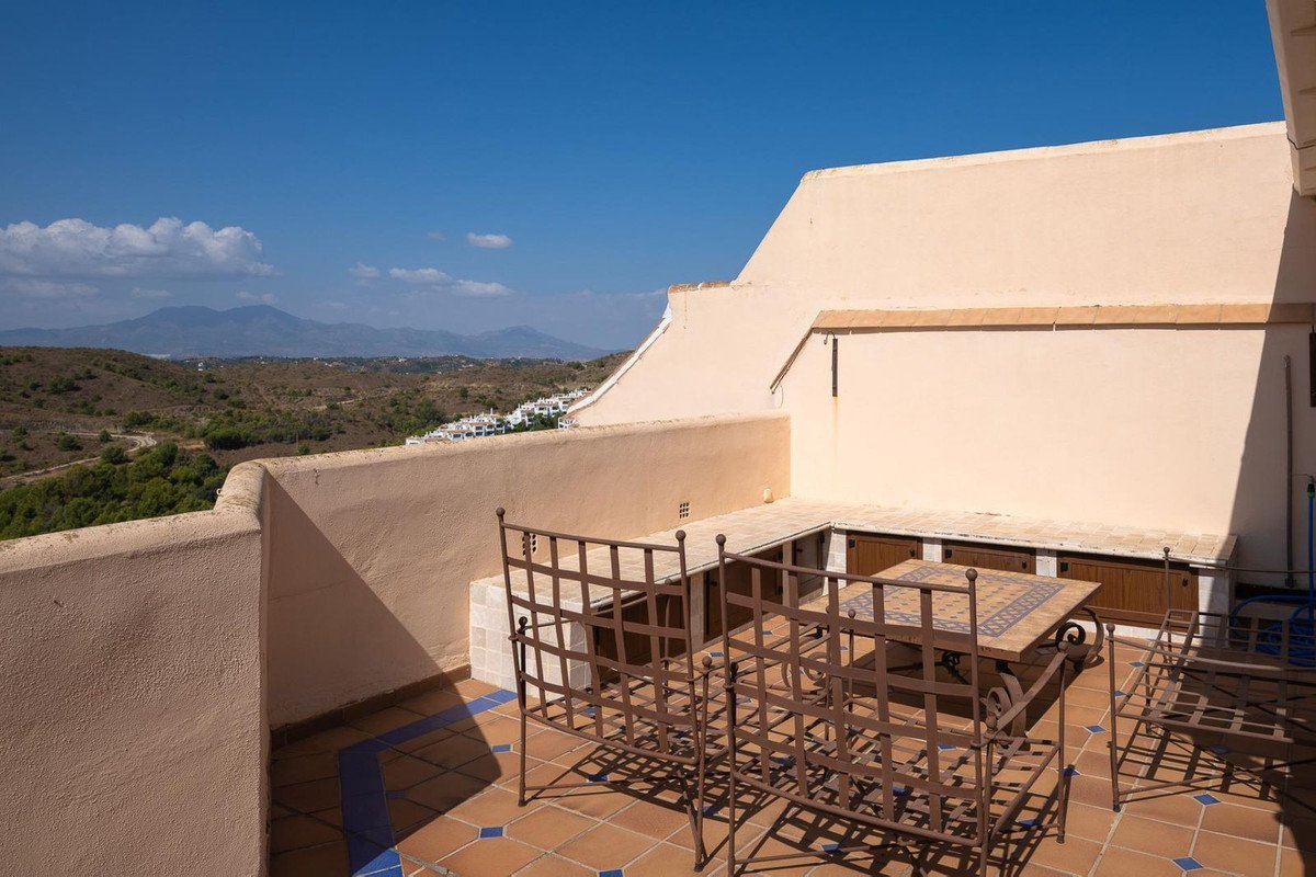 Terrace with wrought iron furniture and dining table, overlooking a distant town and mountains under a clear blue sky.