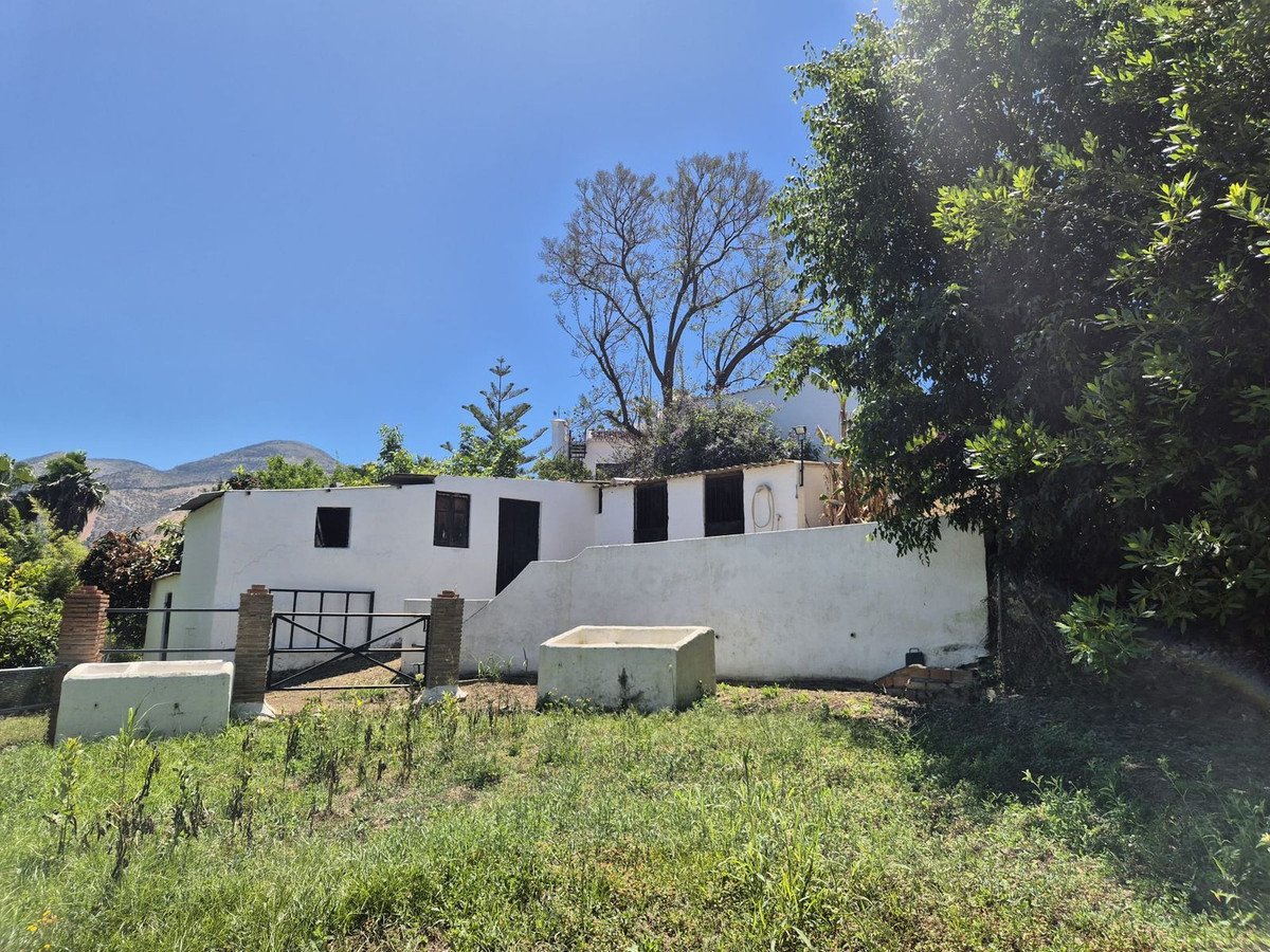 White villa with flat roof, surrounded by greenery and mountains under clear blue sky.