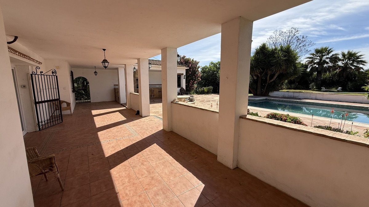 Sunlit patio with tiled flooring and a swimming pool in the background