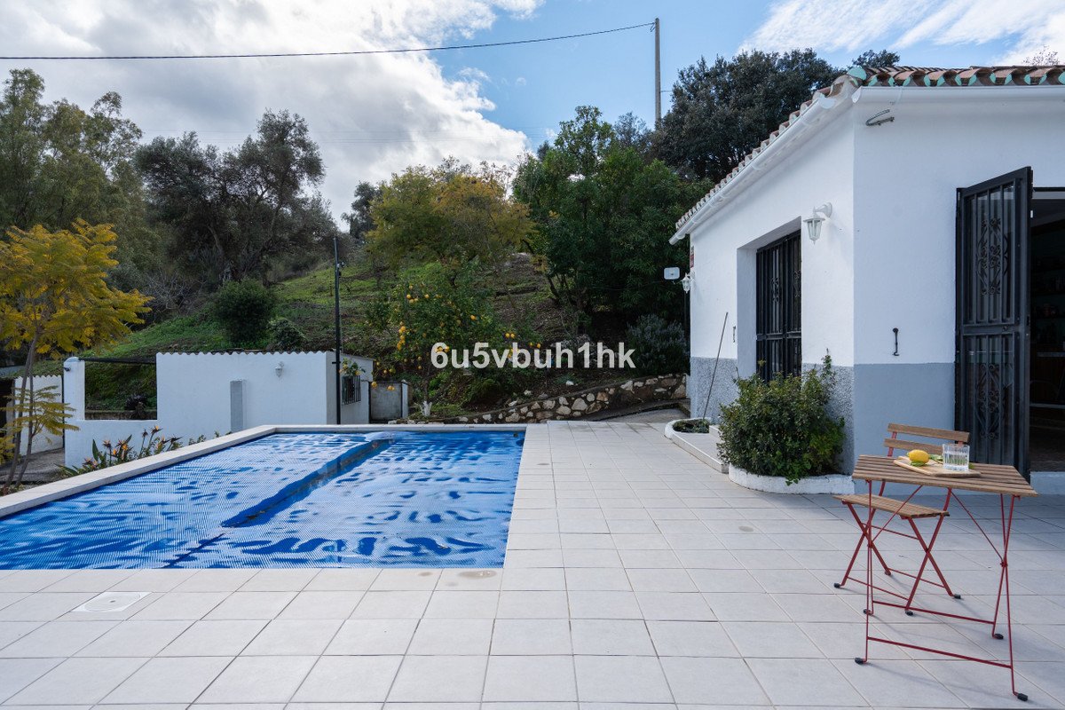 Private swimming pool covered with a blue cover, adjacent tiled terrace with outdoor seating, surrounded by greenery and trees.