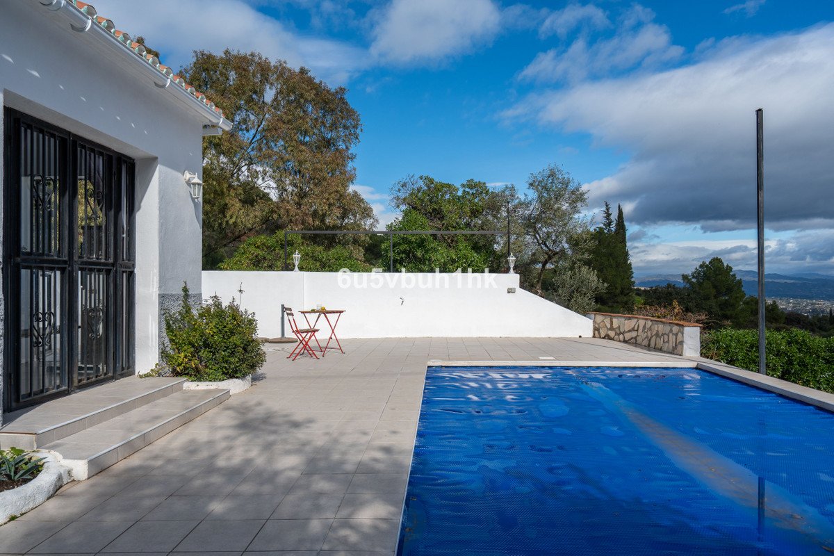 Outdoor terrace with a covered swimming pool, a small table and chairs, and a distant view of a town.