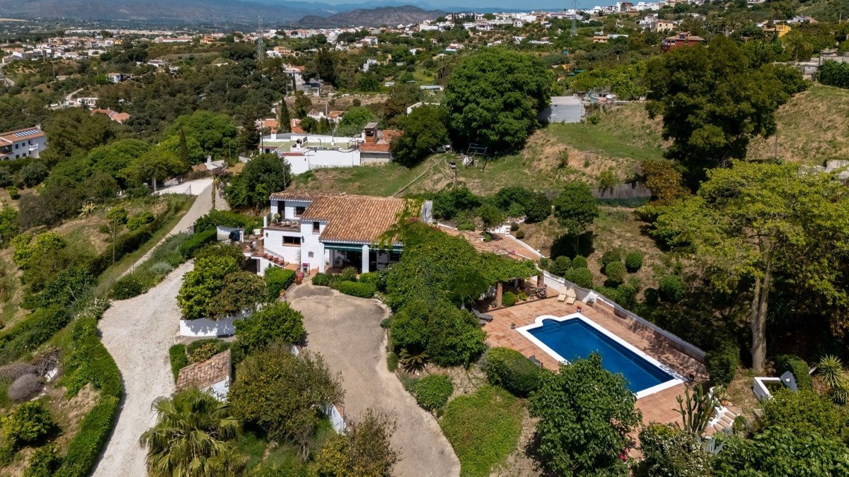 An aerial view of a villa with a swimming pool, surrounded by lush greenery and overlooking a hillside town.