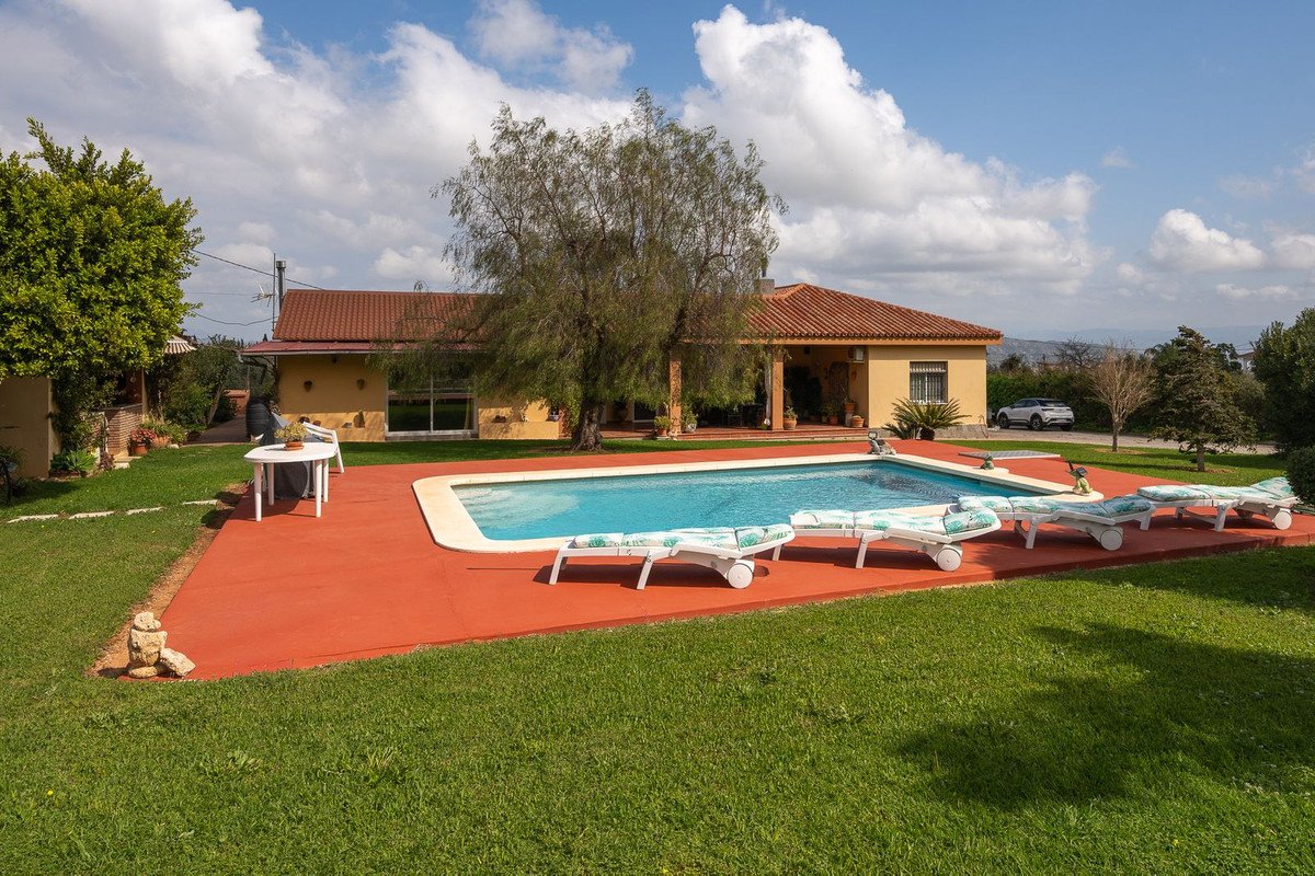 Villa with pool, lounge chairs, and garden under blue sky.