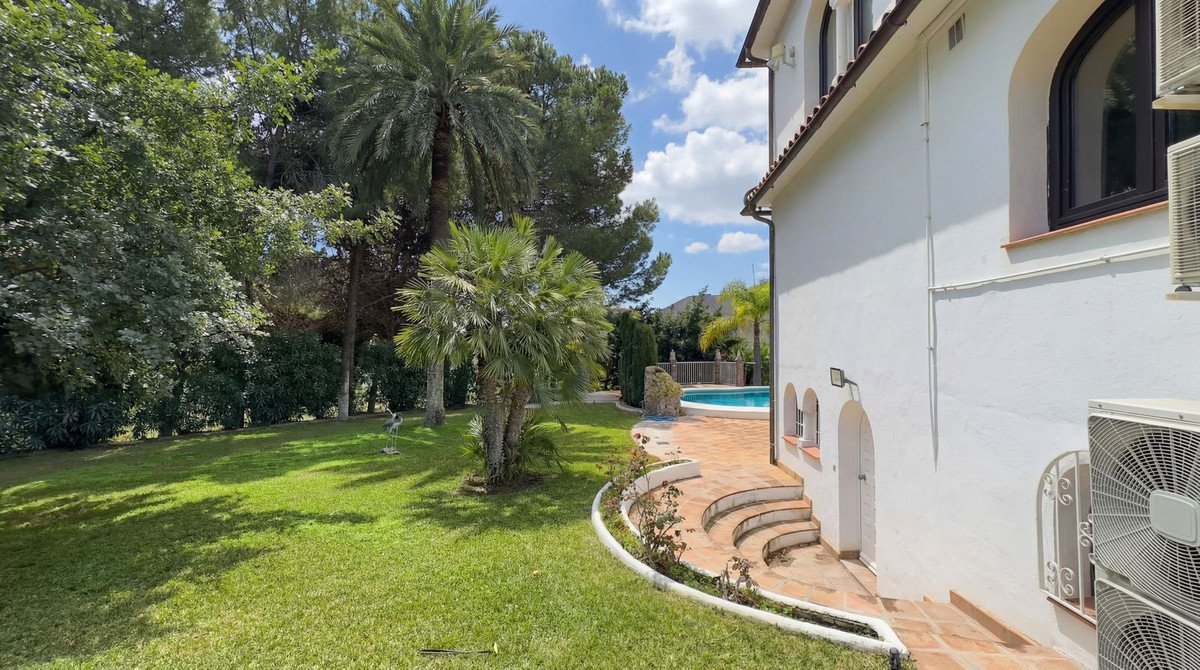 White house with swimming pool and lush garden, sunny outdoor area