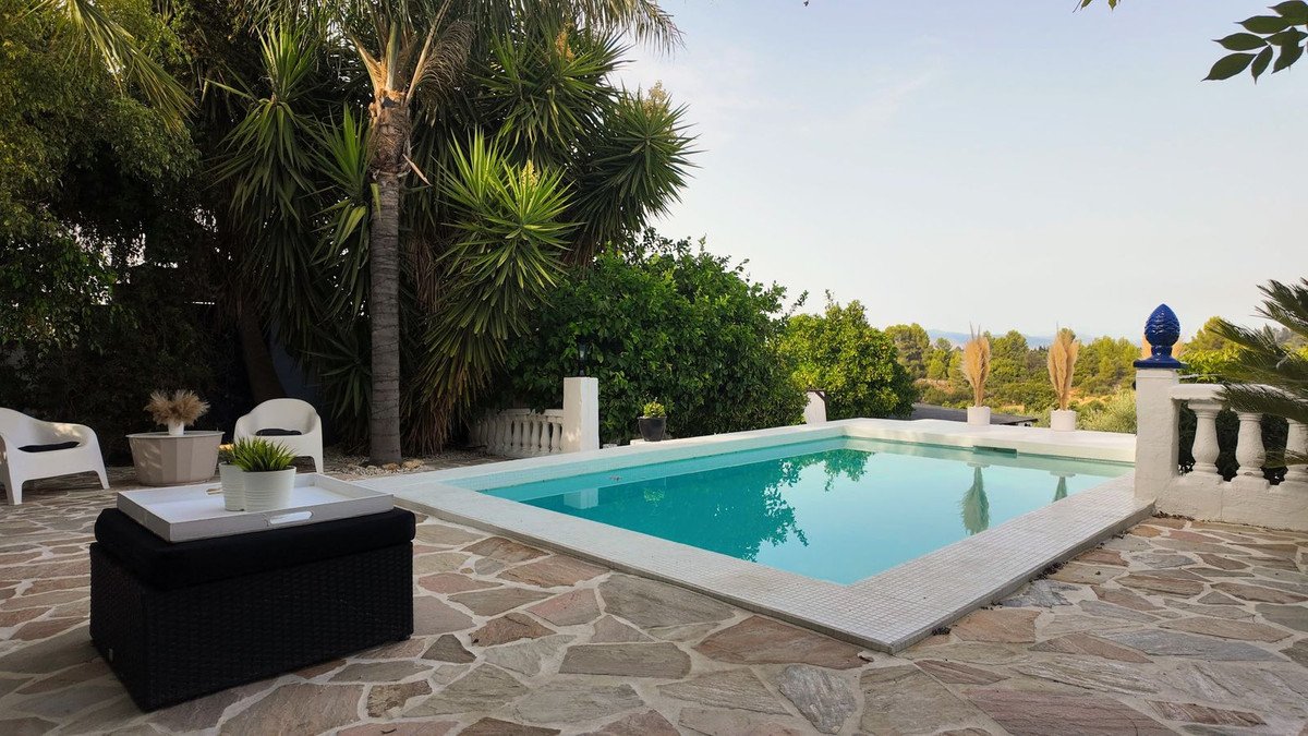 Poolside patio with stone tiles, palm trees, and a view of distant hills.