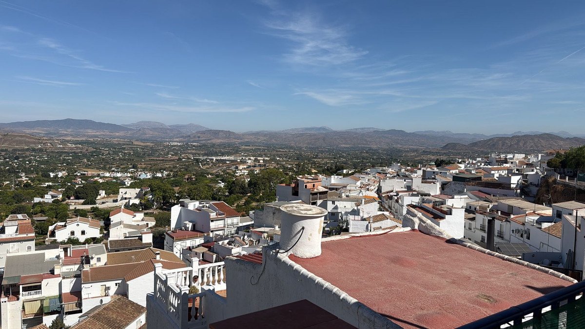 Panoramic view of a white-washed Spanish village with tiled roofs and mountains in the distance under a clear blue sky.