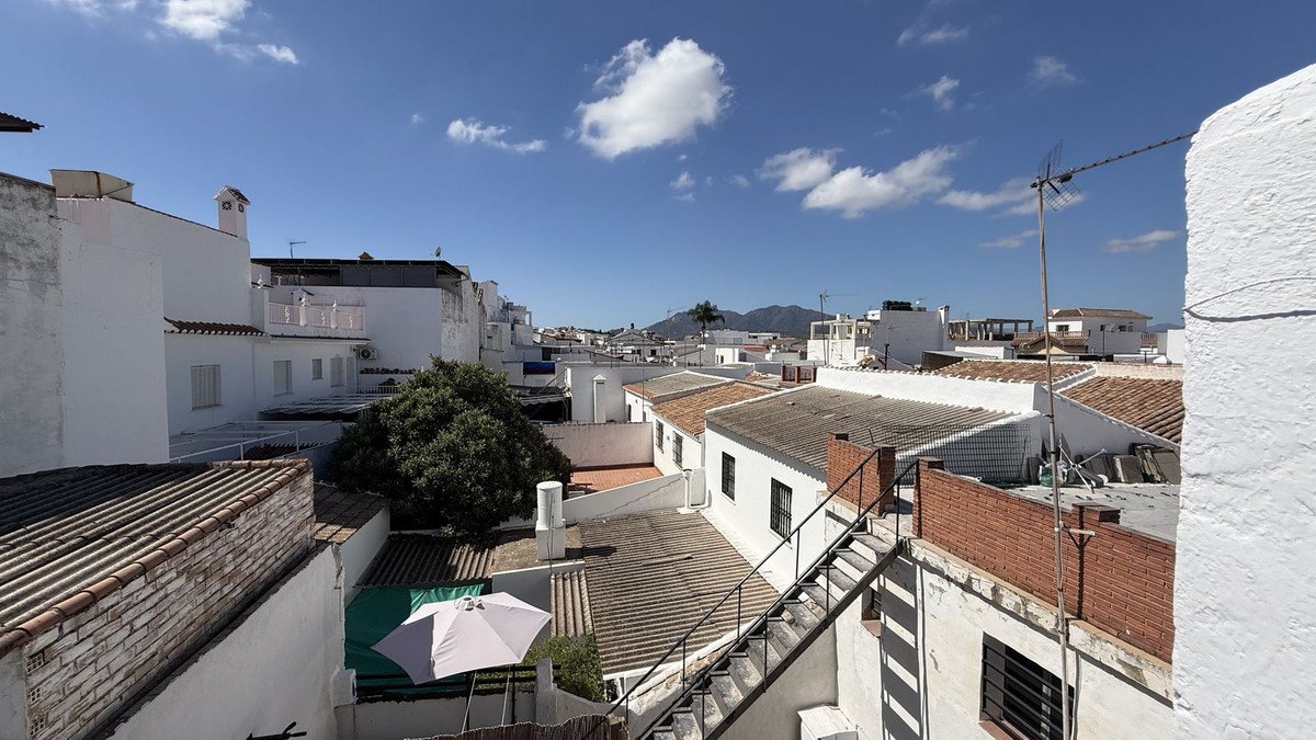 View over rooftops and white buildings towards mountains under a blue sky with scattered clouds.