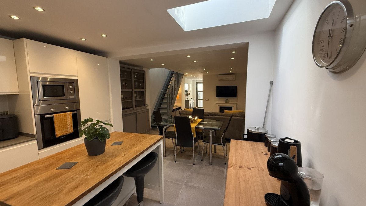 Modern open-plan kitchen, dining, and living area with a skylight, fireplace, and staircase.