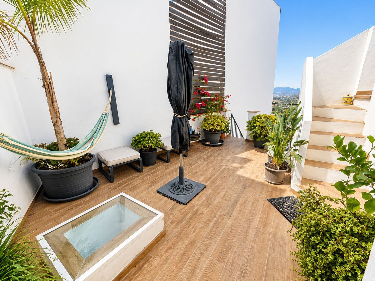 Terrace with a hammock, potted plants, and a distant view of hills and buildings on a sunny day.