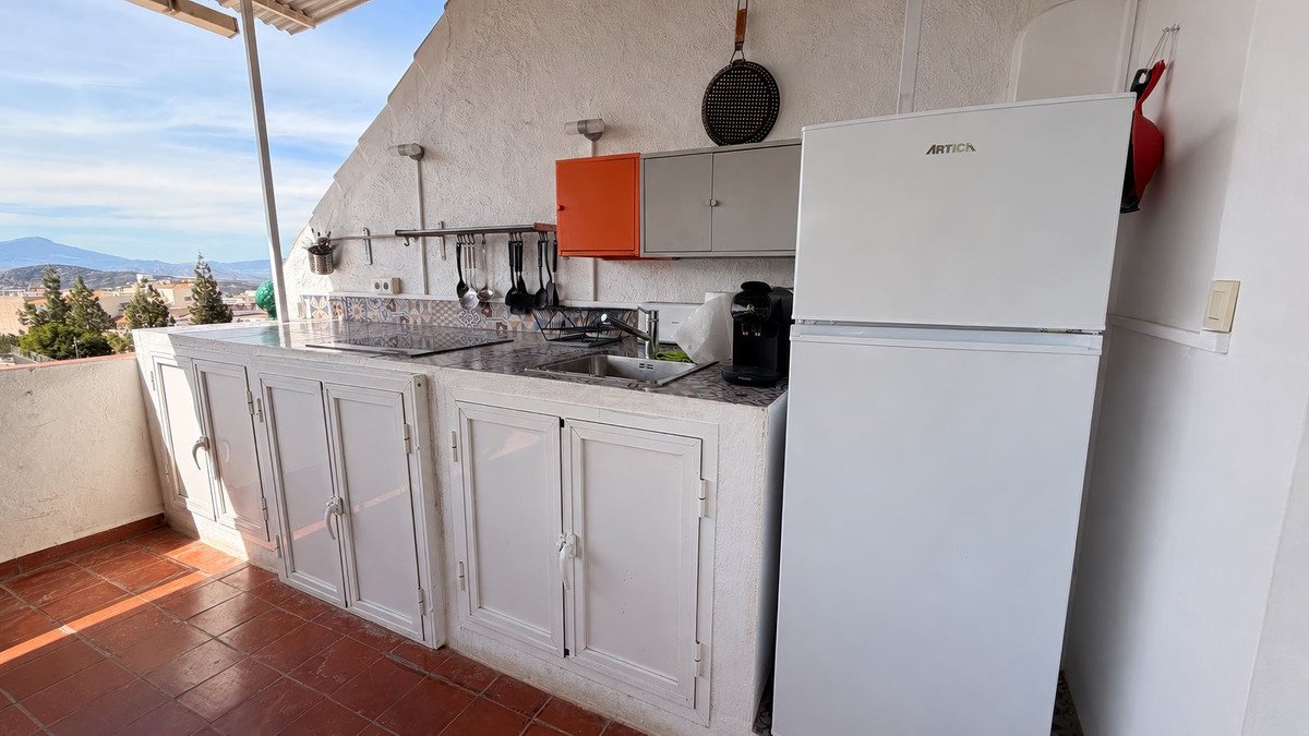 Outdoor kitchen with white cabinets, refrigerator, and mountain view.