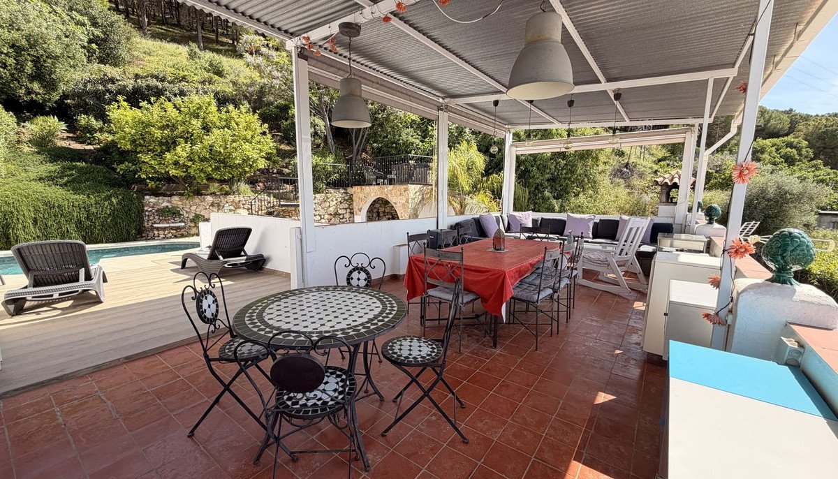 Covered patio with tiled floor, outdoor dining table, lounge seating, and pool view surrounded by greenery.