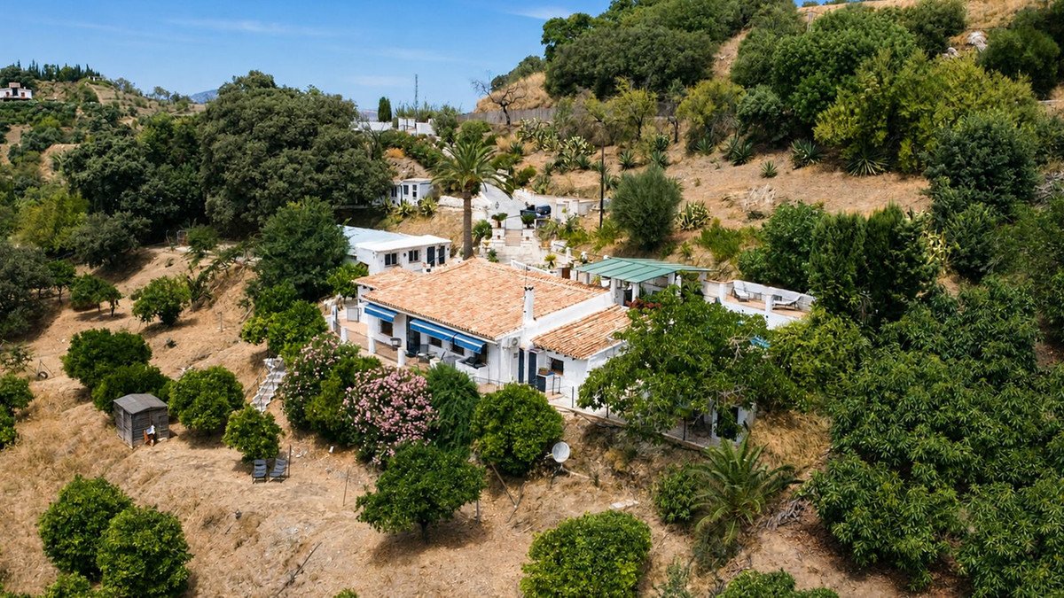 Aerial view of a white villa with terracotta roof, surrounded by lush greenery and trees on a hillside.