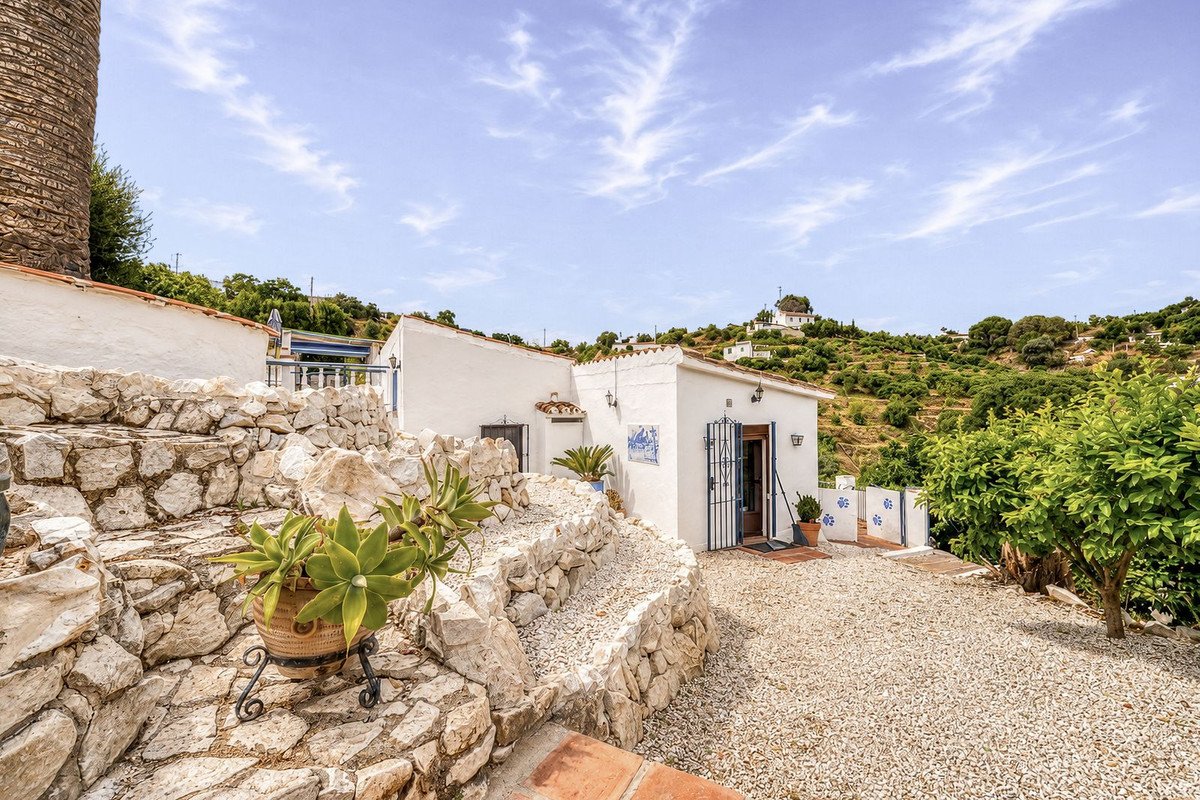 White villa with stone walls, gravel courtyard, and hillside views under a blue sky.