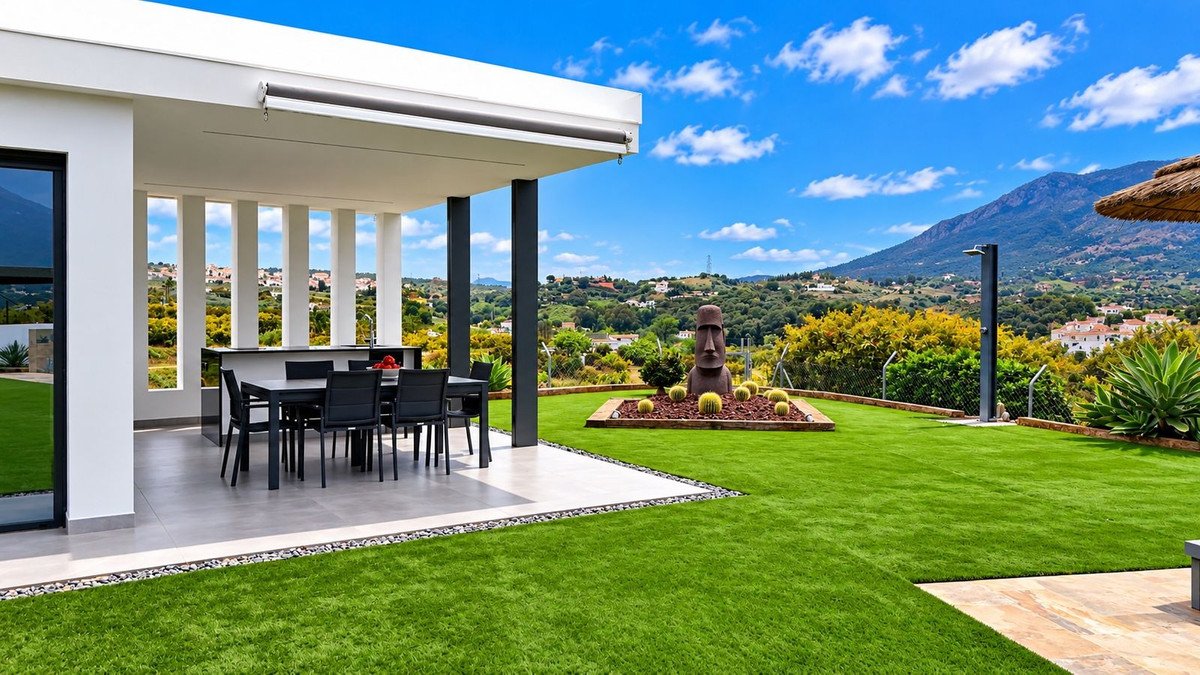 Modern patio with outdoor dining set and a scenic mountain landscape with a unique statue in the garden.
